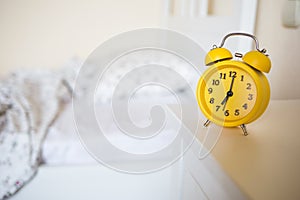 Yellow alarm clock standing on nightstand in background of bed in interior of room. bed`s not made.