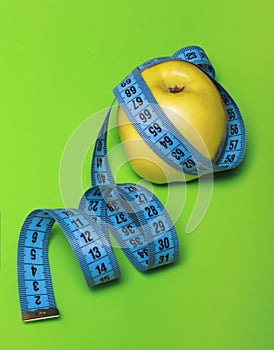 Yellow Apple with blue measuring tape on green background diet and sports concept