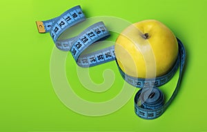 Yellow Apple with blue measuring tape on green background diet and sports concept with a copy of the space