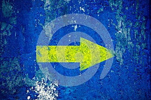 Yellow arrow painted on old grunge and weathered blue wall texture background