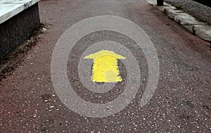 Yellow arrow sign on gray asphalt road showing direction forward