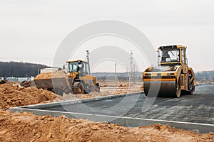 Yellow asphalt compactor at work and orange bulldozer with sand in the background