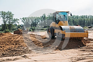 Yellow asphalt paver compactor working on sand at a construction site