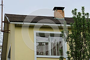 Yellow attic of a private house with a white window under a gray slate roof