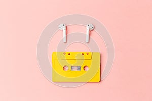 Yellow audio cassette and modern wireless headphones on a pink background. Comparison of old and new technologies