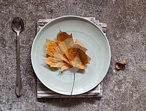 Yellow autumn leaf on a plate on a marble table
