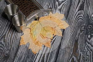 Yellow autumn maple leaves stick out from a jar for an alcoholic drink. Near metal glasses. On pine boards painted black and white