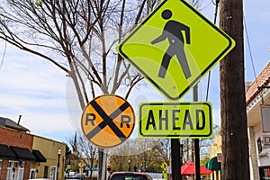 A yellow and back pedestrian walking sign with a yellow and black railroad crossing sign with blue sky and buildings