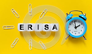 On a yellow background, a blue alarm clock, paper clips and white cubes on which the text is written - ERISA