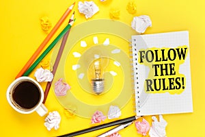 On a yellow background, a cup of coffee, a light bulb, pencils, a notebook with the inscription - FOLLOW THE RULES