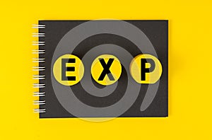 On a yellow background lies a black notebook, yellow wooden circles with the inscription - EXP