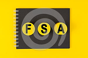 On a yellow background lies a black notebook, yellow wooden circles with the inscription - FSA