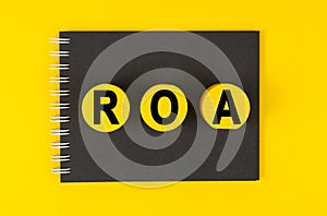 On a yellow background lies a black notebook, yellow wooden circles with the inscription - ROA