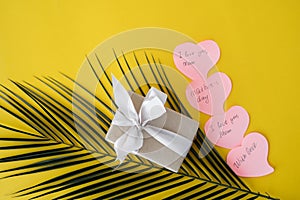 On a yellow background lies a box with a gift, a pink bow, a green palm branch. Sticky leaves with tekt. Free space for text. A