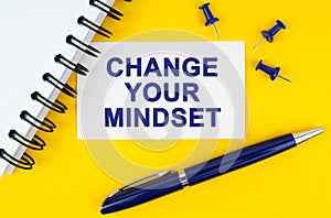 On a yellow background lies a notebook, a pen and a business card with the inscription - CHANGE YOUR MINDSET