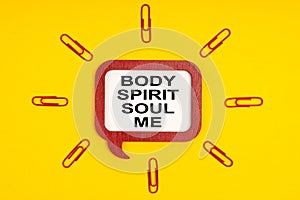 On a yellow background, paper clips and a mental plaque with the inscription - Body Spirit Soul Me