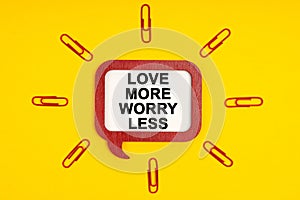 On a yellow background, paper clips and a mental plaque with the inscription - Love More Worry Less