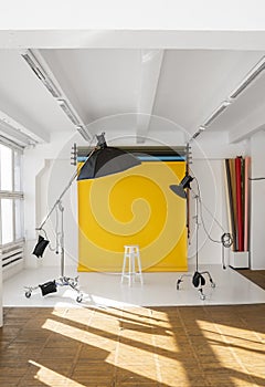 Yellow background roll with a white chair and two professional flash on a c-stands. Sunny daylight photo studio interior