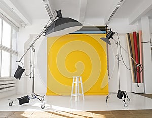 Yellow background roll with a white chair and two professional flash on a c-stands. Sunny daylight photo studio interior