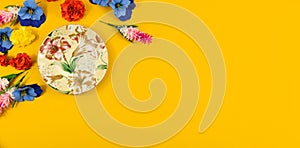 Yellow background and saucer for a cup of tea surrounded by flowers, copy space, flat lay, top view, banner