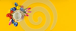 Yellow background and saucer for an empty cup of tea surrounded by flowers, copy space, flat ley, top view banner