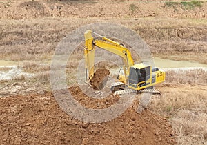 A yellow backhoe is digging a big pond photo