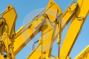 Yellow backhoe with hydraulic piston arm against clear blue sky. Heavy machine for excavation in construction site. Hydraulic