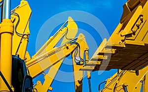 Yellow backhoe with hydraulic piston arm against clear blue sky. Heavy machine for excavation in construction site. Hydraulic