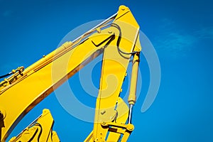 Yellow backhoe with hydraulic piston arm against clear blue sky. Heavy machine for excavation in construction site. Hydraulic