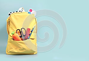 Yellow backpack with accessories, school supplies in schoolbag on empty space green background.Knapsack with education objects