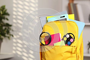Yellow backpack with different school stationery indoors, closeup. Space for text