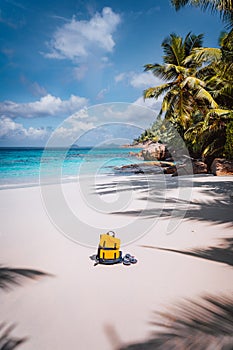 Yellow backpack and flip flops on beautiful tropical sandy beach. Palm trees and blue sky. Holiday vacation concept