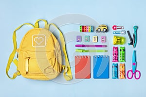 Yellow backpack with school supplies - notebook, pens, eraser rainbow, numbers isolated on blue background