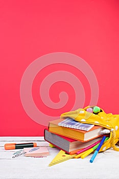 Yellow backpack with white polka dots with different colorful stationery on table. Bright Red background. Back to school