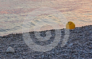 A yellow ball on a pebble beach at sunset.