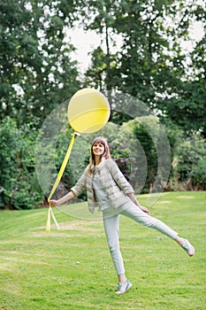With a yellow balloon. Happy beautiful young studient girl walking in european garden. She is looking at the camera