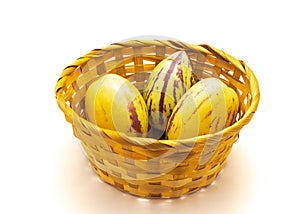 Yellow bamboo basket with three Pepino melons or Solanum muricatum isolated on white