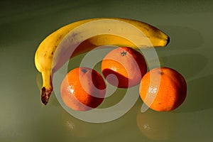 Yellow banana and orange color clementines groupped in closeup view on reflective glass