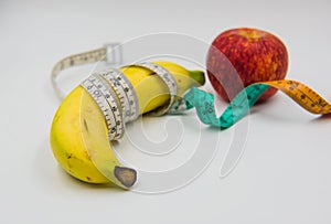 Yellow banana and red apple Measuring tape wrapped around on white background