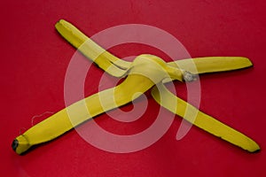 Yellow banana skin on a red background. Concept for warning of slippery surfaces and danger of slipping. Close-up