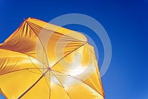 Yellow beach umbrella against the blue sky, protection from the scorching sun