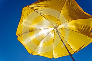 Yellow beach umbrella against the blue sky, protection from the scorching sun