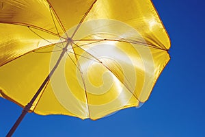 Yellow beach umbrella against the blue sky, protection from the scorching sun
