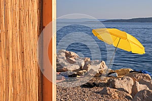 Yellow beach umbrella on summer coast. Sea beach with sun parasol is waiting for tourists on Sunset.