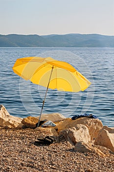 Yellow beach umbrella on summer coast. Sea beach with sun umbrella is waiting for tourists on Sunset.