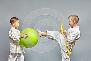 With a yellow belt, an athlete beats a kick on a green ball on a gray background