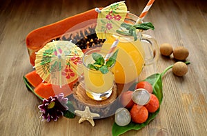 Yellow beverage in glass vessels surrounded by tropical fruits