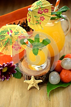 Yellow beverage in glass vessels surrounded by tropical fruits