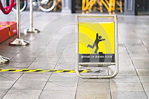 Yellow beware of uneven floor sign board on tile floor