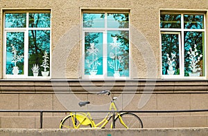 Yellow bicycle in front of building facade with windows decorated with imitated flowers and blue sky in reflection